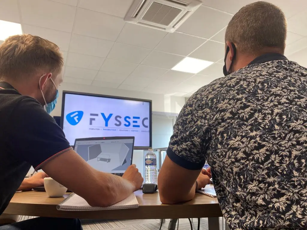 deux personnes discutant devant un ordinateur avec comme fond d'écran le logo fyssec